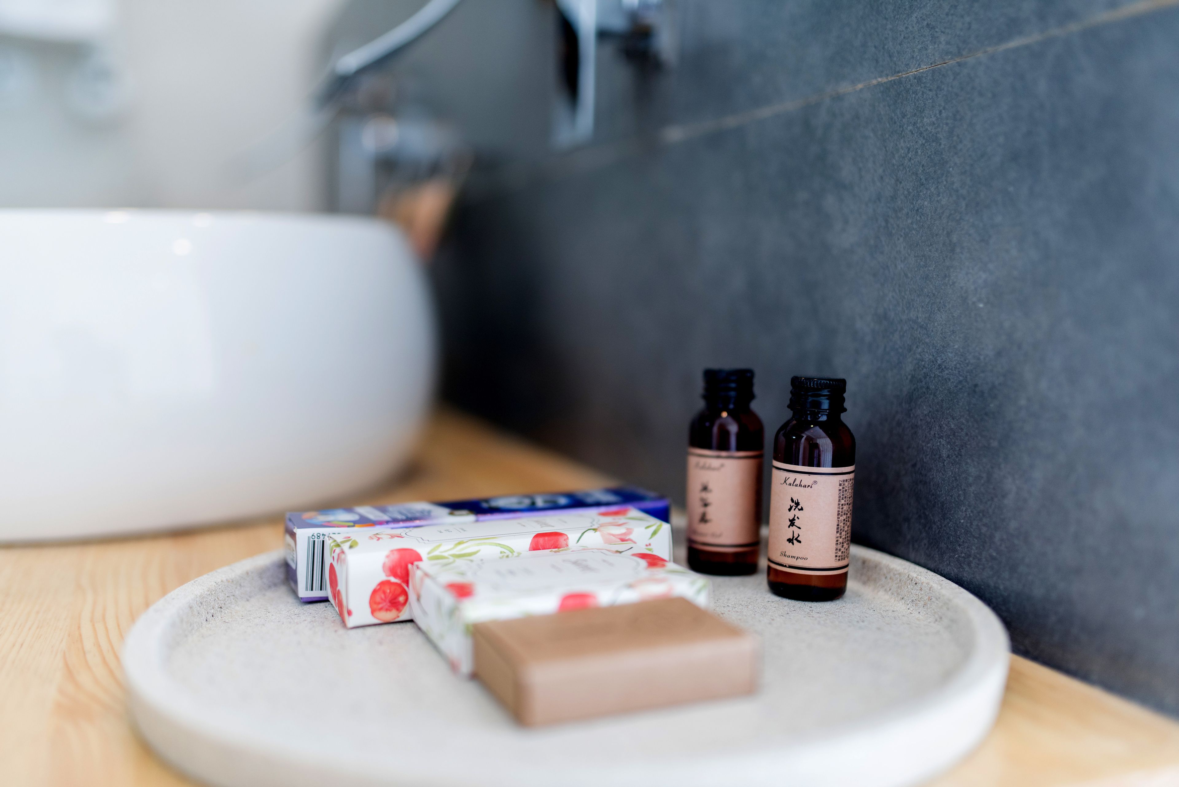 A bathroom sink with a white basin, a soap bar, and two small bottles of liquid soap on a round ceramic tray.
