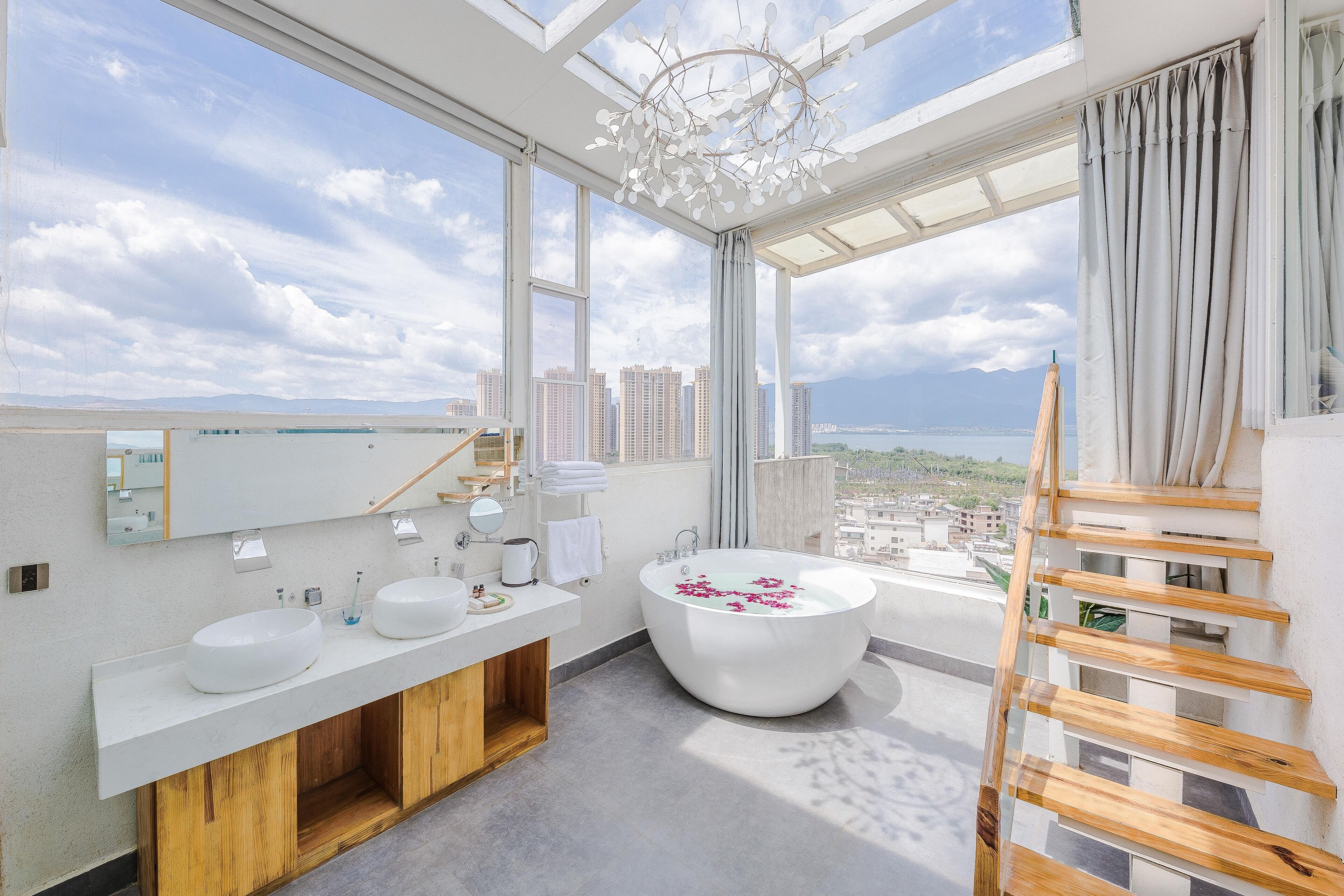 A modern bathroom with a large bathtub, two sinks, and a view of the city and sea.