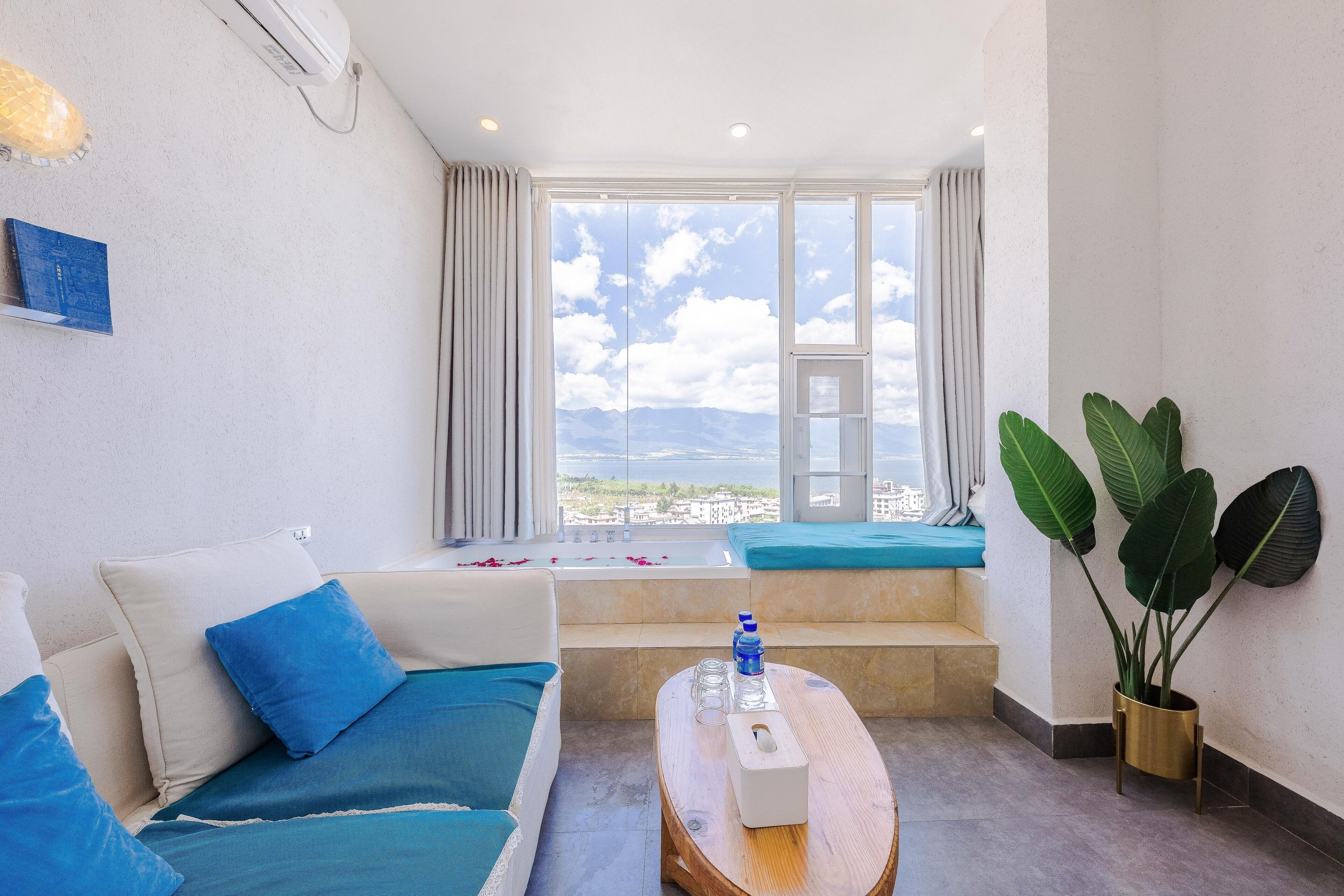 Una habitación de hotel con un ventanal grande, un sofá, una mesita de centro y una planta en maceta.