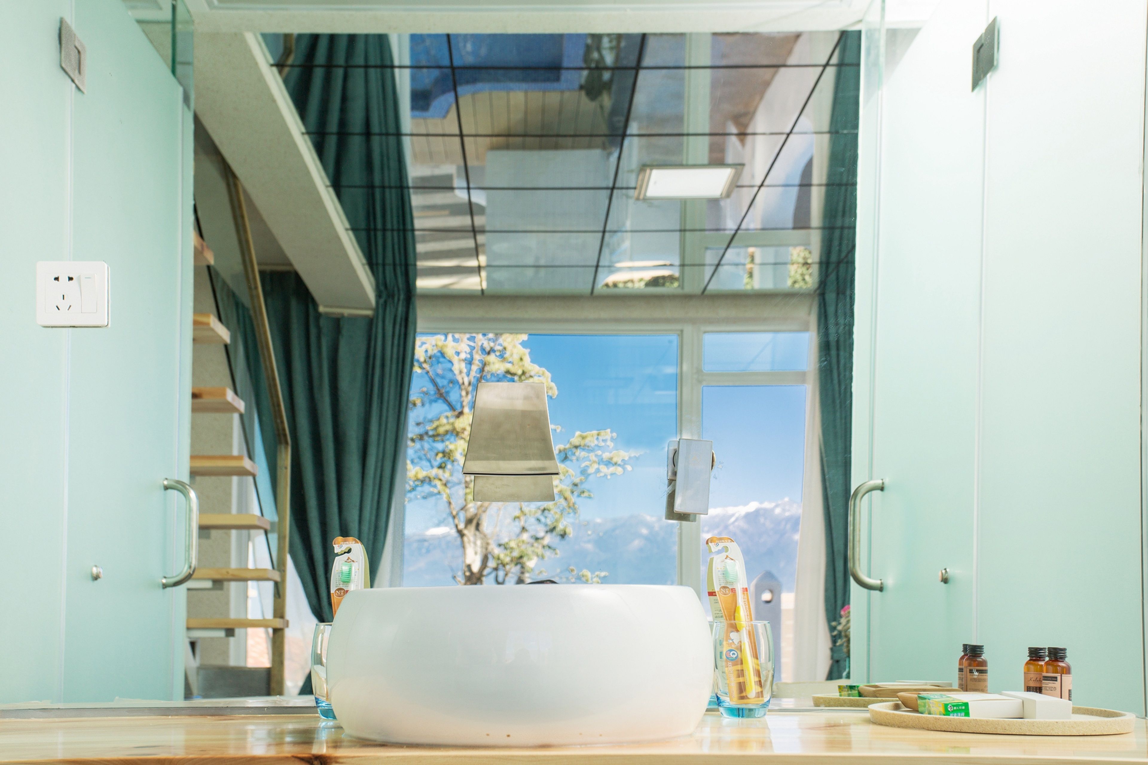 A bathroom with a large sink, a mirror, and a window with a view of a tree and mountains.