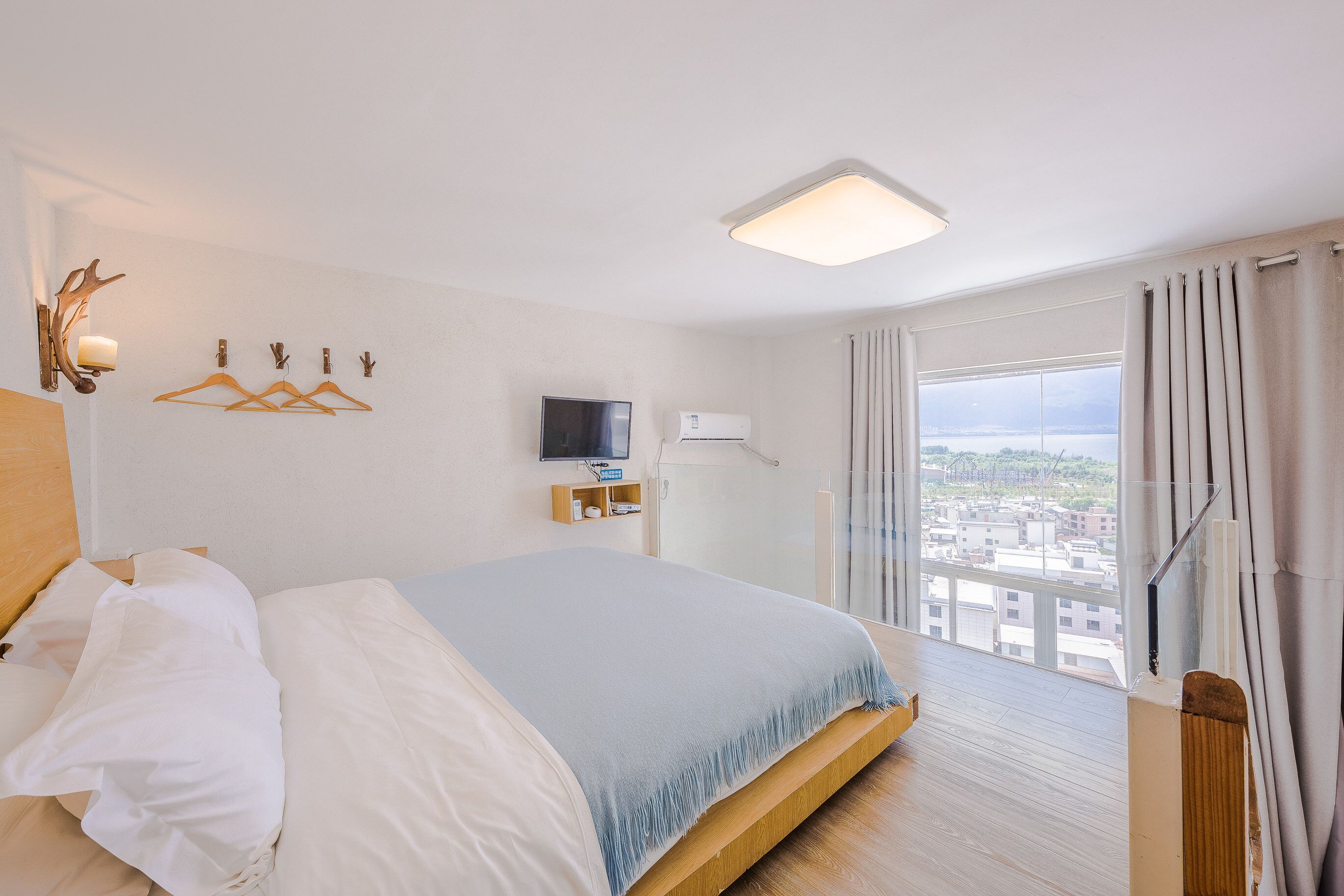 A hotel room with a bed, a TV, a window with curtains, and a view of buildings.