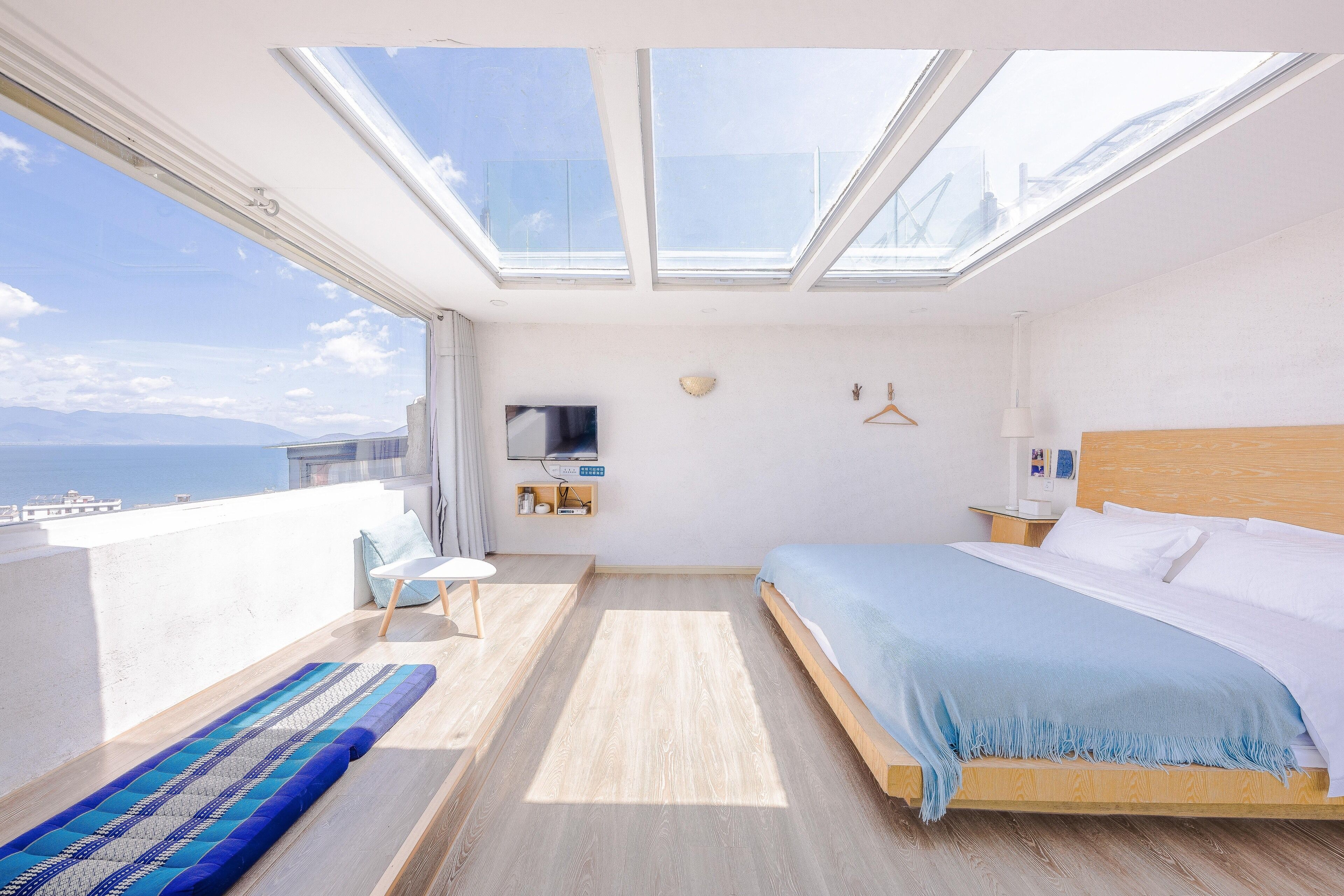 Un dormitorio con un tragaluz grande, una cama, una mesita de noche, una silla y vista al mar.
