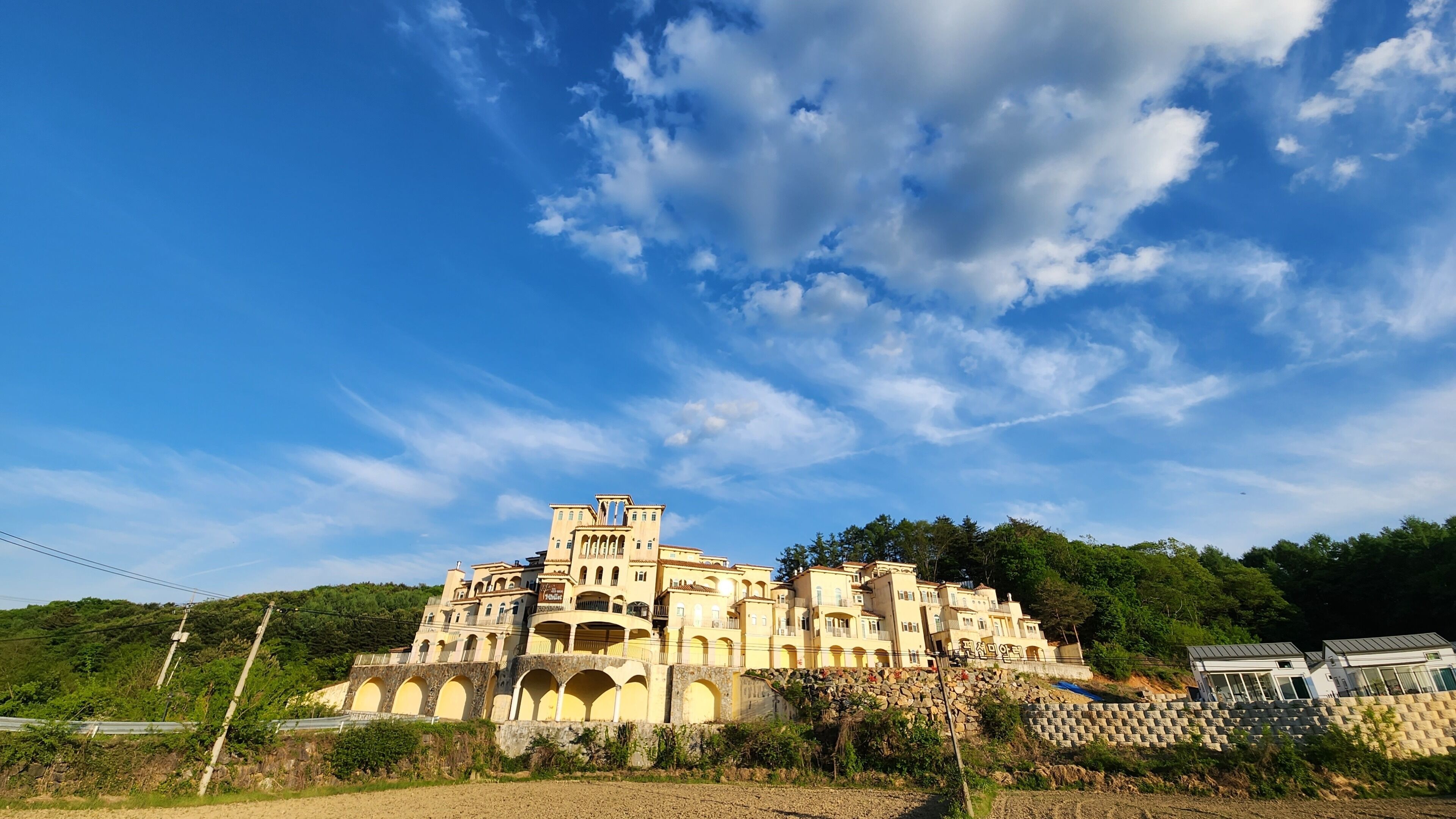 A large, multi-story building with arched windows and balconies, set against a clear blue sky with scattered clouds.