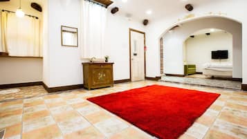 Habitación de hotel con alfombra roja, un armario de madera, un espejo, una puerta, un televisor y un sofá verde.