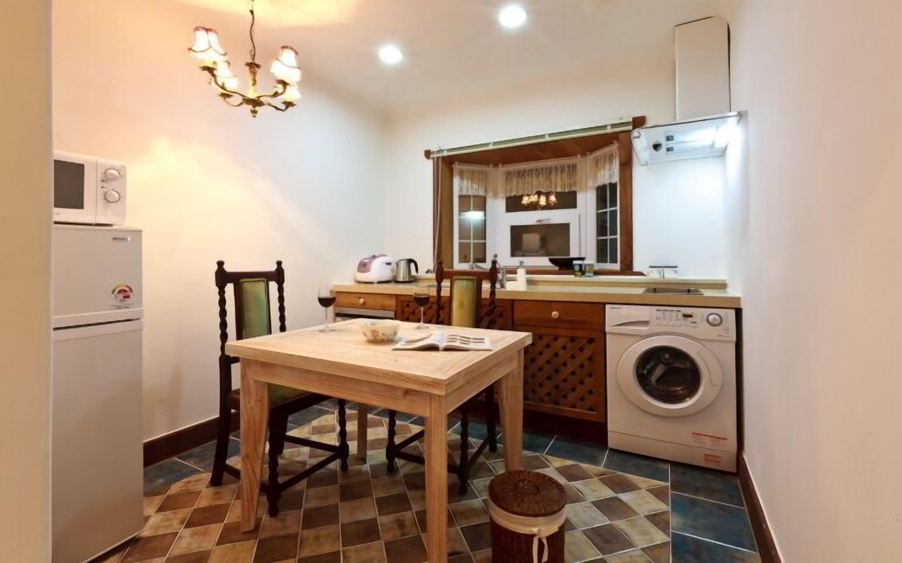 A compact kitchen with a dining table, a washing machine, a microwave, and a chandelier.
