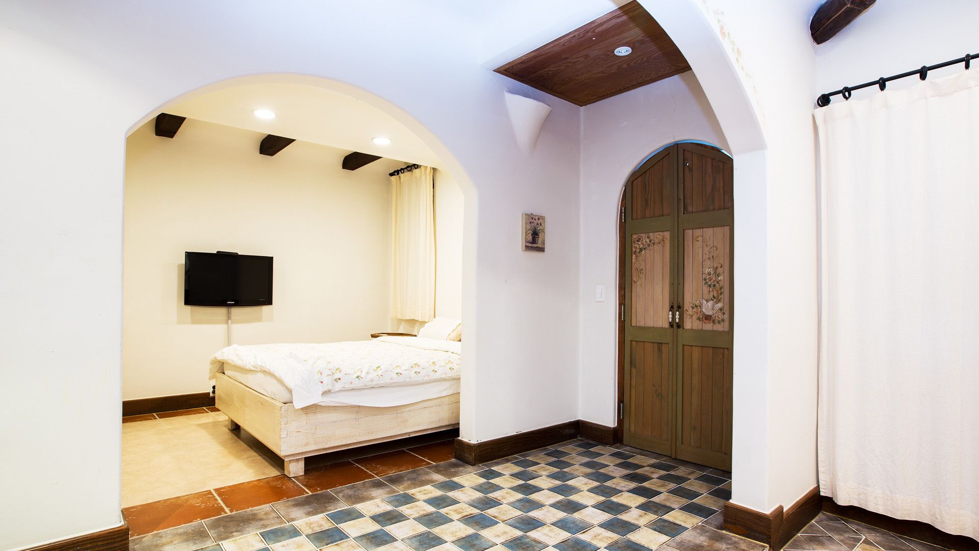 Une chambre à coucher avec un lit, un téléviseur, une porte en bois et un sol carrelé.