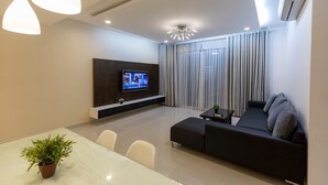 Una sala de estar moderna con un televisor de pantalla plana, un sofá oscuro, una mesa de comedor con sillas y una planta en maceta.