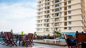 Un hotel de varios pisos con balcones, un área de piscina con sillas de descanso y vista al mar.