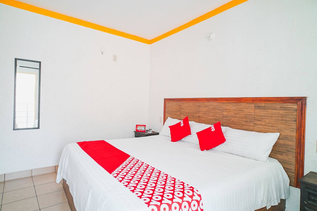 A neatly made bed with a red and white patterned bedspread, a wooden headboard, and two red pillows.