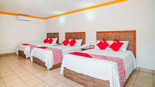 Ein Hotelzimmer mit drei Betten, jeweils mit einem hölzernen Kopfteil und roten Kissen.