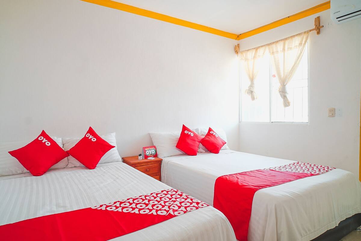 A hotel room with two beds, each with red and white bedding, a wooden nightstand, and a window with curtains.