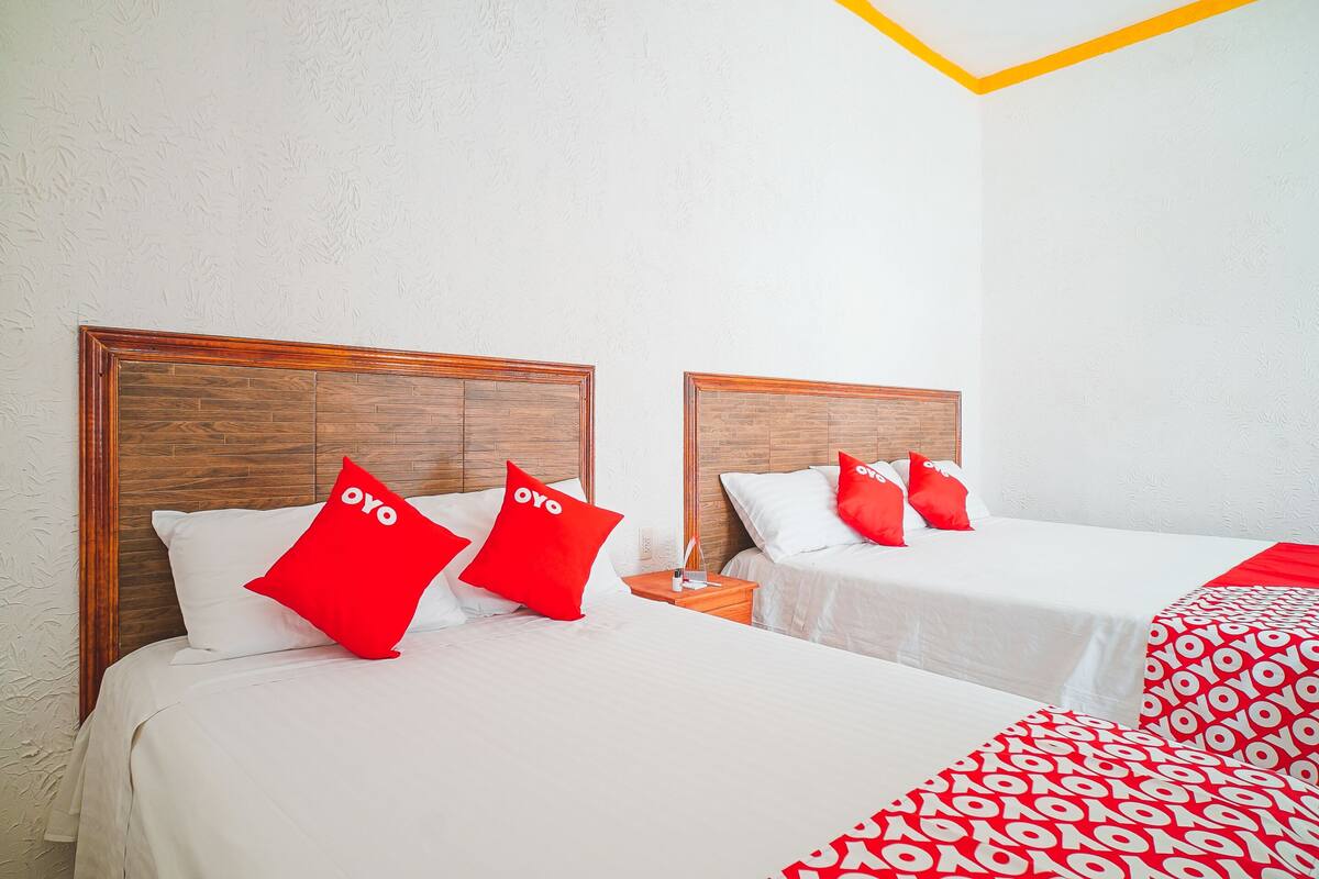 Two beds with wooden headboards, white bedding, and red pillows with the word "oyo".