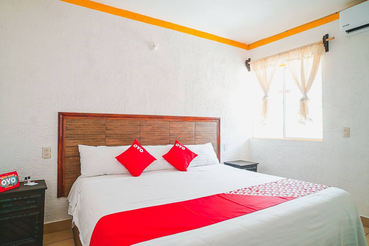 A hotel room with a wooden headboard, white walls, and a red and white bedspread.