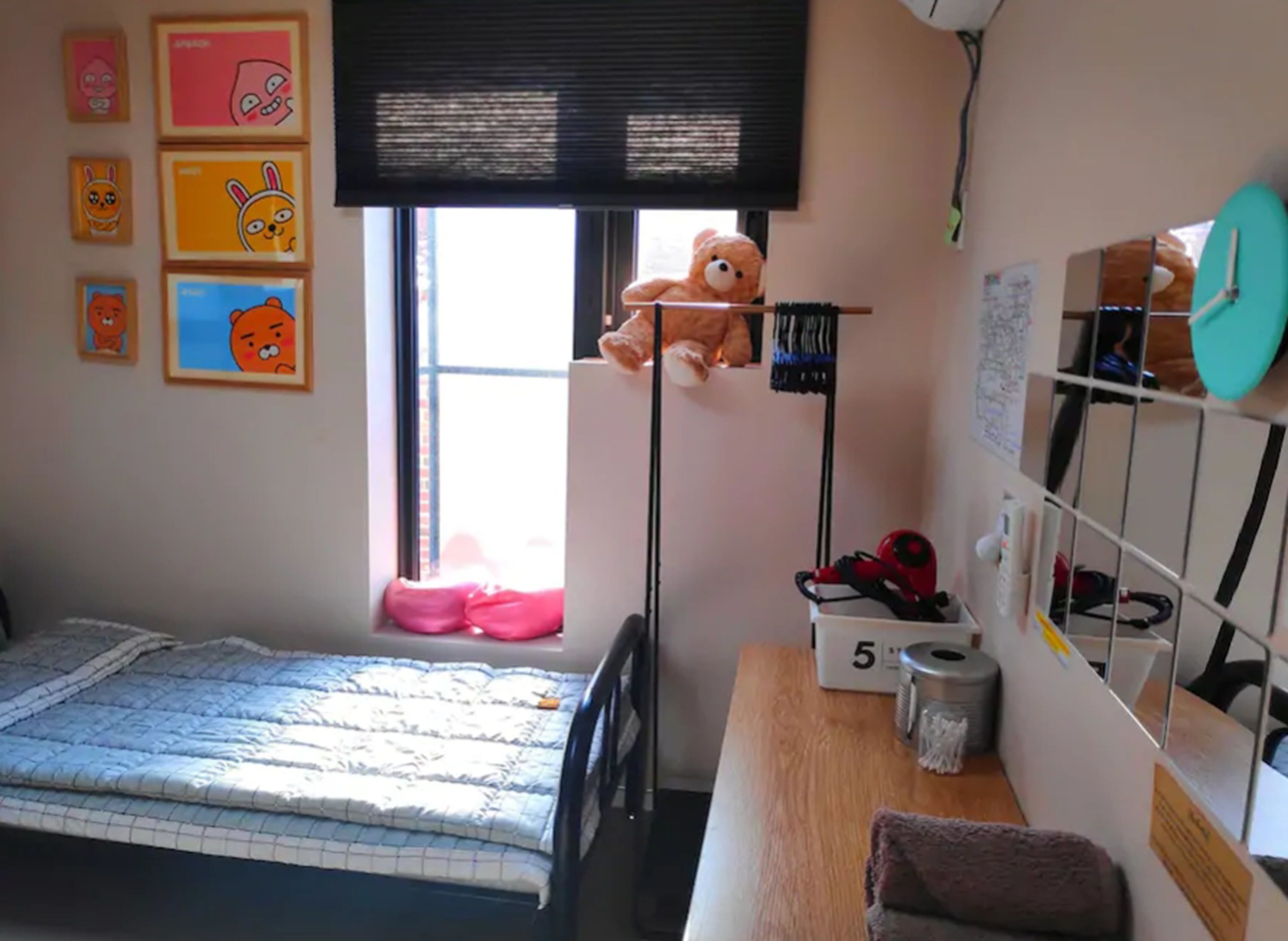 Una camera da letto con un letto, una scrivania con una sedia, un orsetto sullo scaffale e una finestra con persiane.