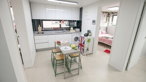 A modern kitchen with white cabinets, a dining area with stools, and a small washing machine. - Kuki House (Seoul)