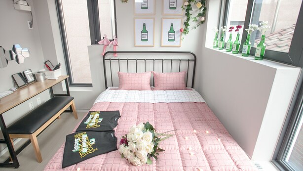 A neatly arranged bedroom with a bed, bedside table, and a window with decorative bottles. - Kuki House (Seoul)