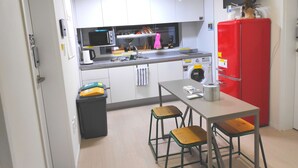 A compact kitchen with white cabinets, a red refrigerator, a microwave, a sink, and a small dining area with stools. - Kuki House (Seoul)