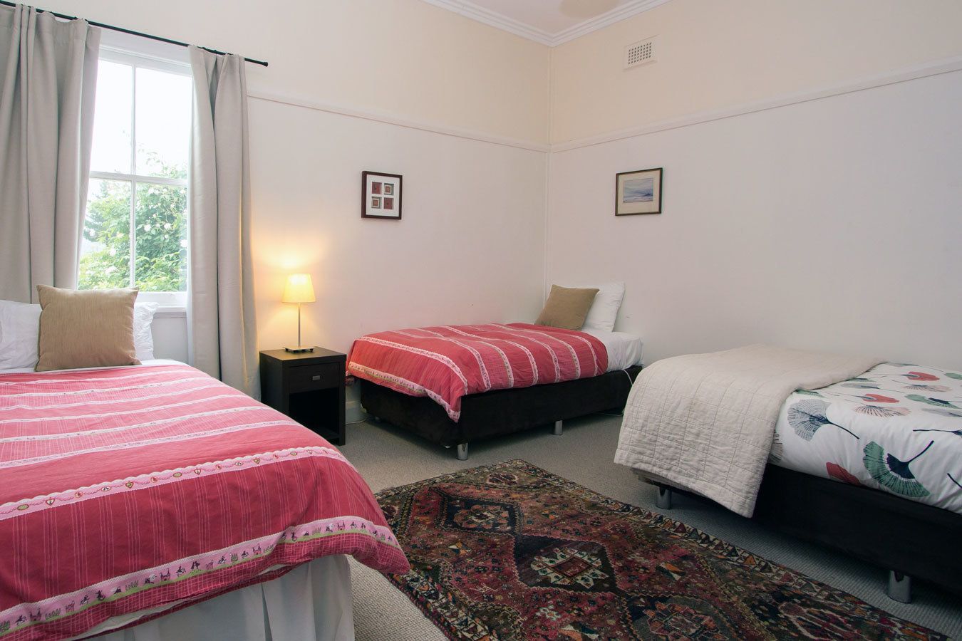 A bedroom with two beds, a nightstand, a lamp, and a patterned rug.