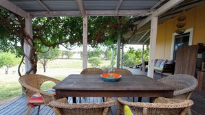 A covered outdoor patio with a wooden table and wicker chairs. - Lone Pine Farmhouse (Meroo)