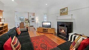 A living room with a fireplace, a television, and a sofa with patterned cushions. - Lone Pine Farmhouse (Meroo)