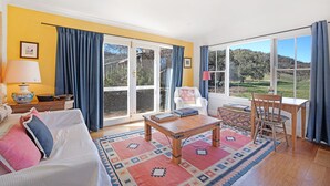 A spacious living room with a large window, a sofa, a coffee table, and a dining area. - Lone Pine Farmhouse (Meroo)