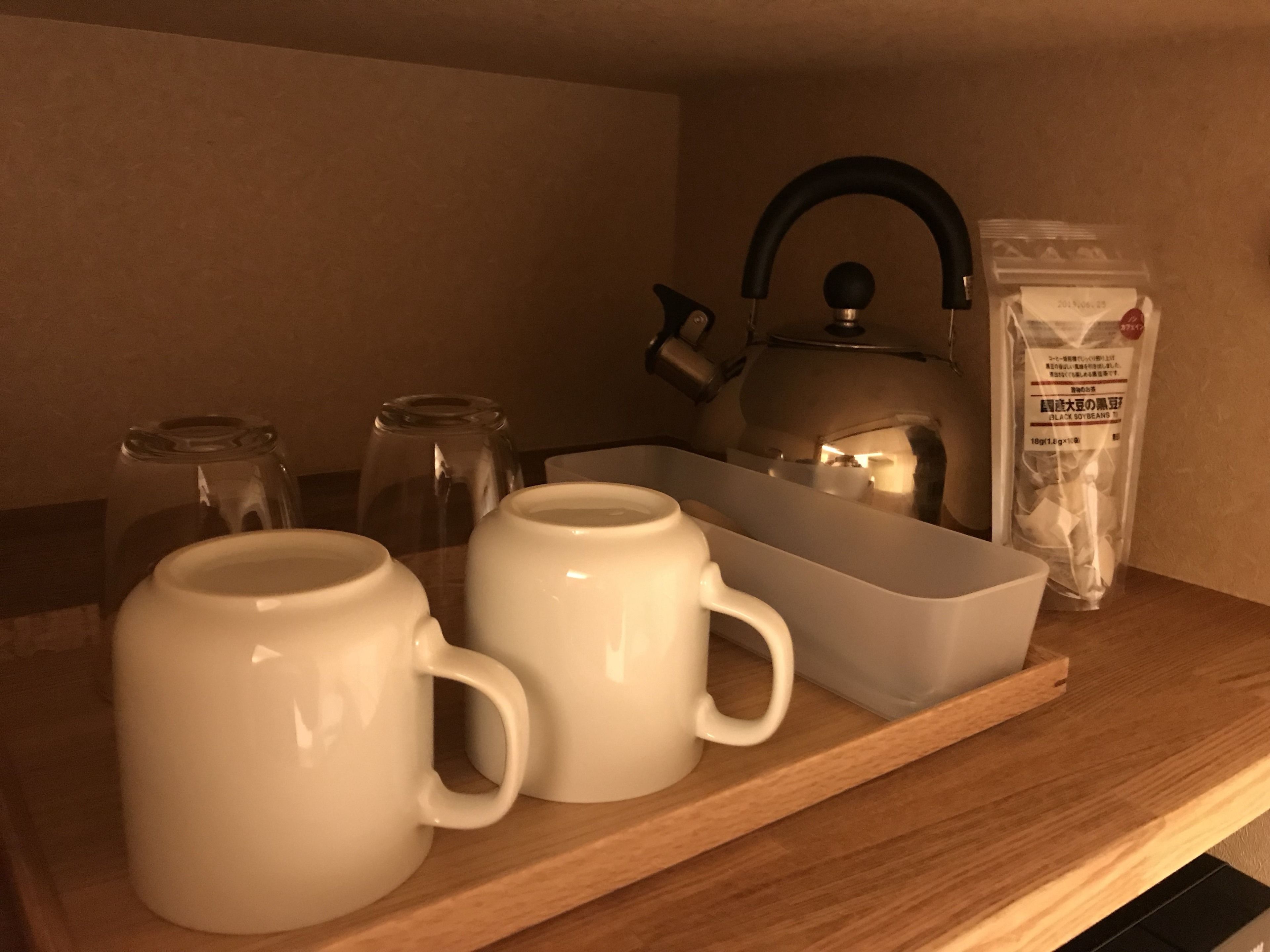 A kitchen area with a kettle, two white mugs, a glass jar, and a bag of black soybeans on a wooden countertop.