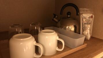 A kitchen area with a kettle, two white mugs, a glass jar, and a bag of black soybeans on a wooden countertop.