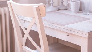 Une chaise en bois blanche avec un dossier, une table blanche et un pichet blanc posé sur la table.