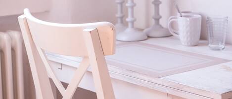 Una silla de madera blanca con respaldo, una mesa blanca y una jarra blanca sobre la mesa.