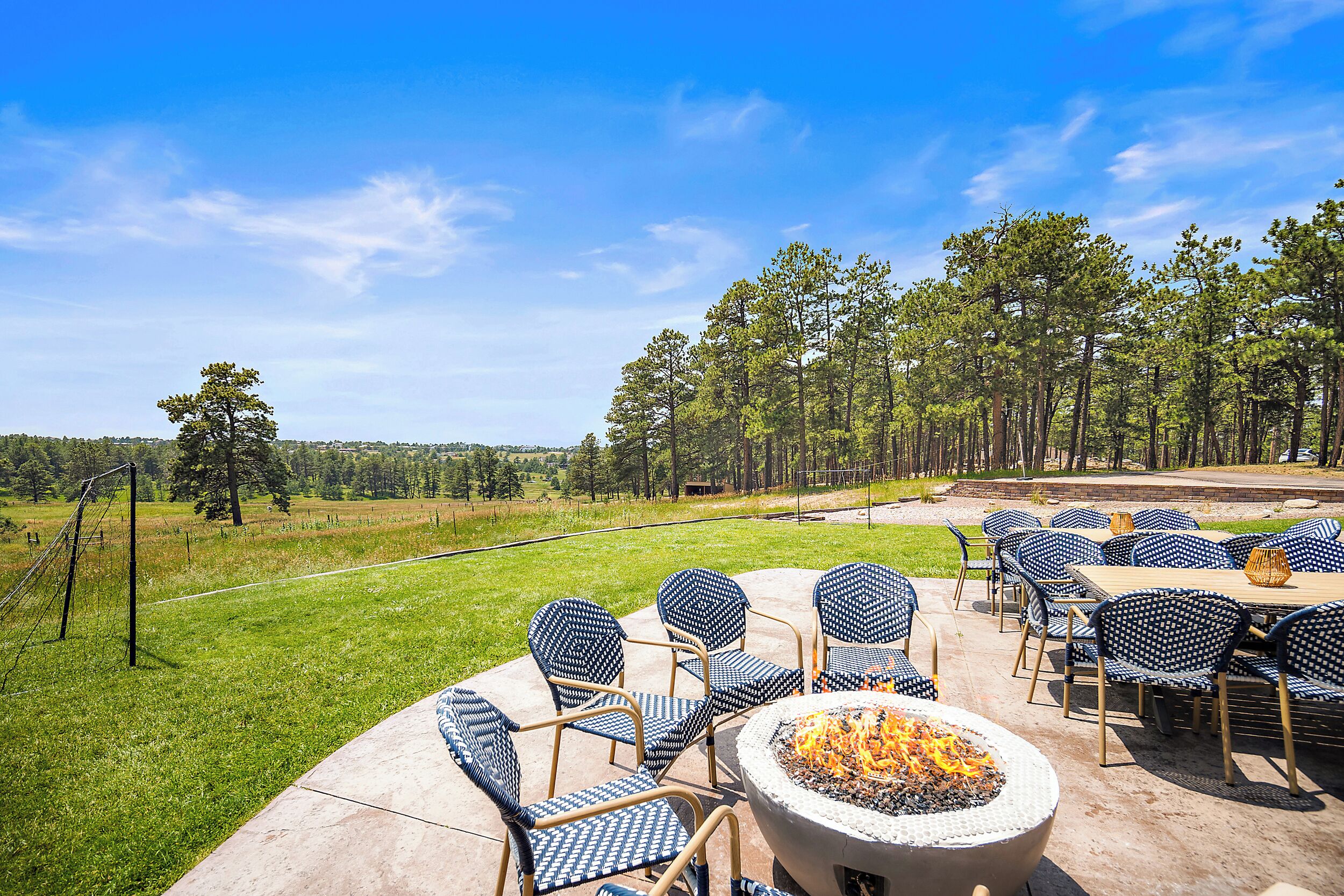 An outdoor patio with chairs and a fire pit, overlooking a grassy area and trees.