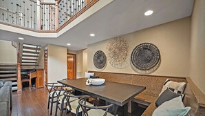 Un vaste espace dédié à la salle à manger, avec une longue table et de nombreuses chaises, un escalier en bois et des œuvres d’art décoratives murales.