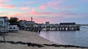 A waterfront promenade with a pier extending into the water, featuring a series of buildings and a lighthouse in the background. - Stylish Dog-Friendly Condo - West End on Comm St (Provincetown)