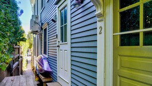 A wooden deck with a bench, a purple kayak, and a house with light blue siding and a green garage door. - Stylish Dog-Friendly Condo - West End on Comm St (Provincetown)