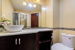 A bathroom with a white sink, a toilet, and a shower. There is a mirror above the sink and a wooden door in the background. - Cozzy Seaview Apartment (Ho Chi Minh City)