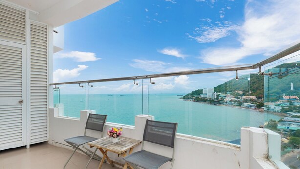 A balcony with two chairs and a table, overlooking a coastal view with buildings and a clear sky. - Cozzy Seaview Apartment (Ho Chi Minh City)