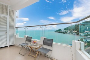 A balcony with two chairs and a table, overlooking a coastal view with buildings and a clear sky. - Cozzy Seaview Apartment (Ho Chi Minh City)