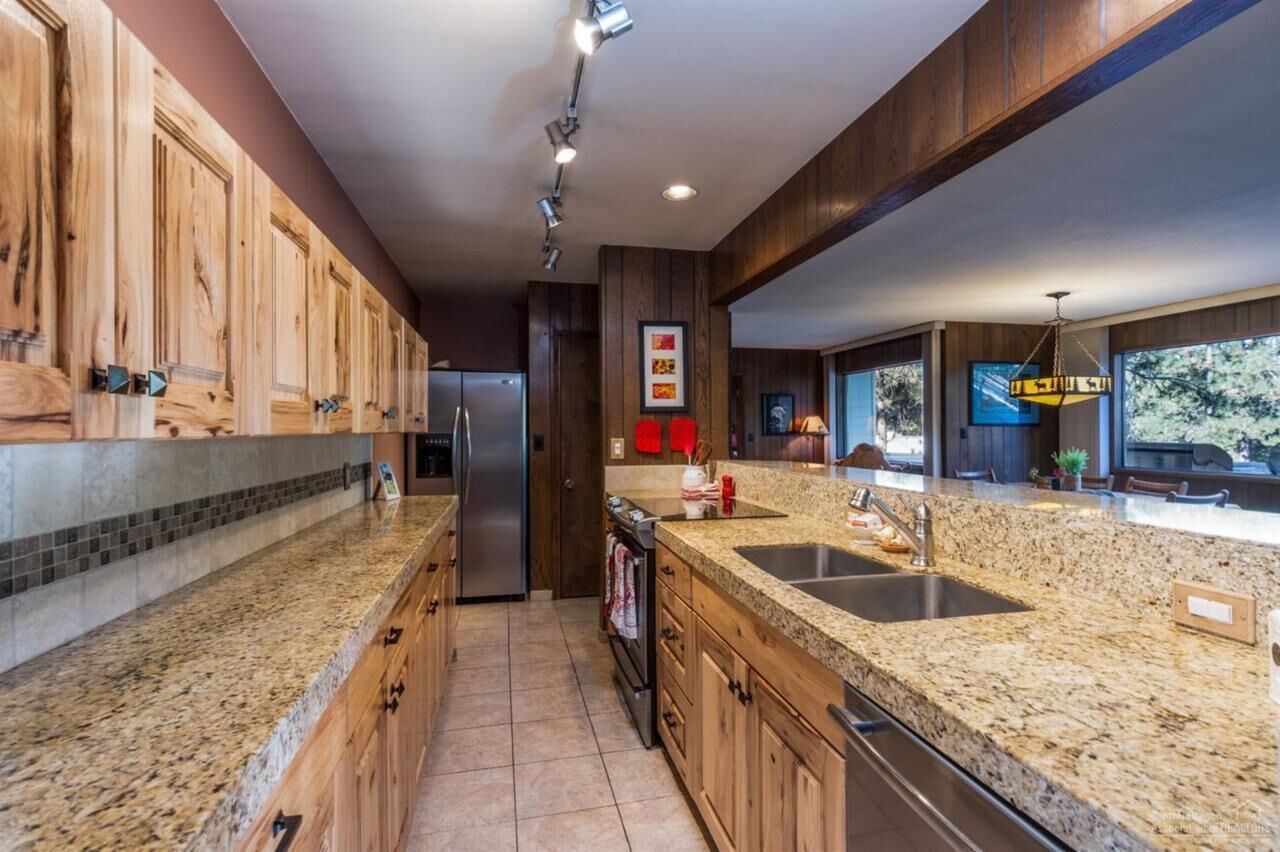 Una cocina moderna con armarios de madera, encimeras de granito, electrodomésticos de acero inoxidable y un amplio ventanal que proporciona luz natural.