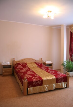 A neatly made bed with a red and gold bedspread, two bedside tables with lamps, a potted plant, and a ceiling light fixture. - Hotel Ekran (Lviv)