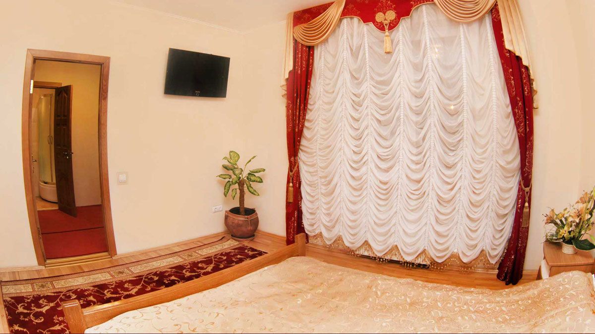 Un dormitorio con una cama grande, una planta en maceta, un televisor en la pared y una cortina roja y blanca.