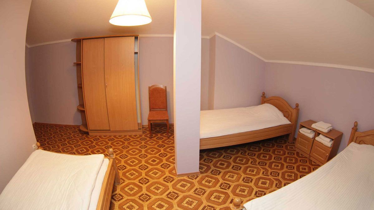 Una habitación pequeña y acogedora con dos camas individuales, un armario de madera, una silla y una lámpara.