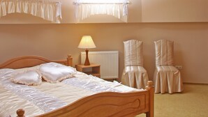 A bedroom with a wooden bed, a nightstand with a lamp, a radiator, and two chairs. - Hotel Ekran (Lviv)