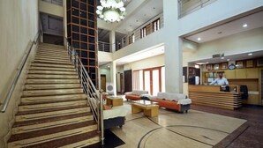 A spacious lobby with a staircase, a reception desk, and a seating area. - Hotel Shrinathinn (Nathdwara)