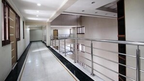 A corridor with a metal railing, white walls, and a marble floor. - Hotel Shrinathinn (Nathdwara)