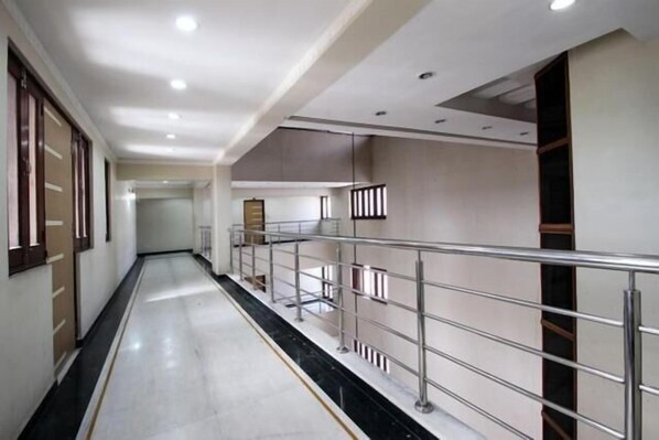 A corridor with a metal railing, white walls, and a marble floor. - Hotel Shrinathinn (Nathdwara)