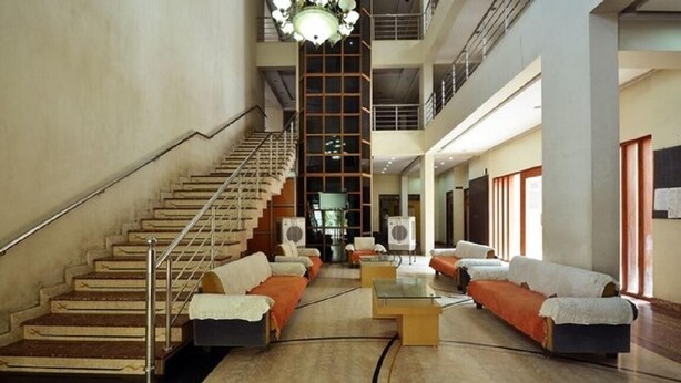 A spacious lobby with a central staircase, seating areas, and a high ceiling with a chandelier. - Hotel Shrinathinn (Nathdwara)