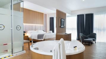 Una habitación de hotel moderna con una bañera grande, una cama con cabecero de madera, un box de ducha de vidrio y una zona de estar con una silla.