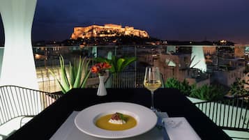 A table with a dessert and a glass of wine, overlooking a cityscape with a historic building.