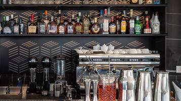 Een bar met flessen drank, een koffieapparaat en baraccessoires.