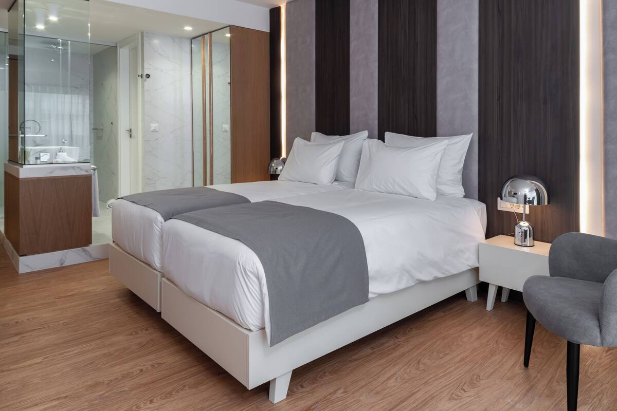 A modern bedroom with a large bed, bedside tables, a chair, and a glass-enclosed shower area.