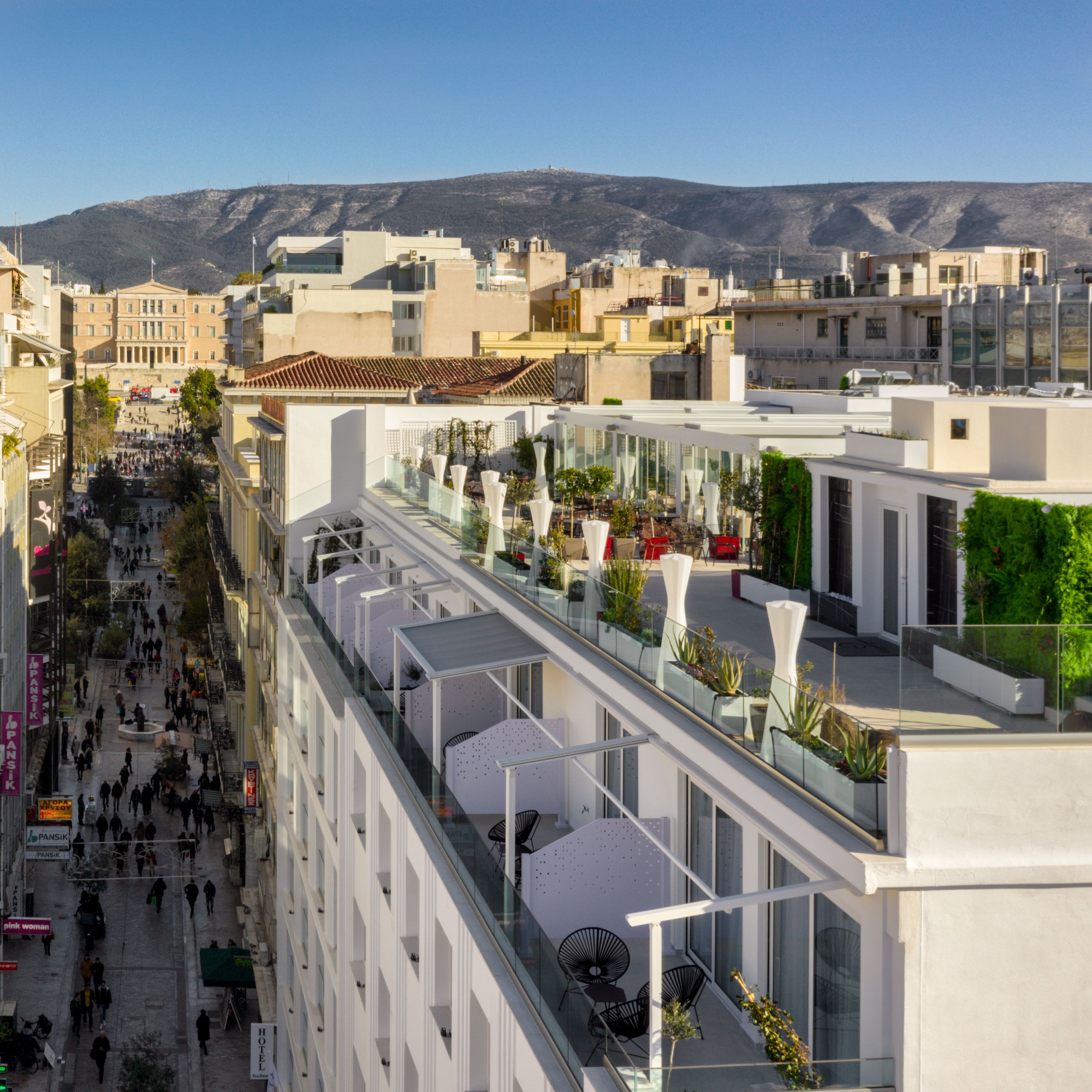 Ein modernes Hotel mit Glasfassade, Sitzgelegenheiten im Freien und Blick auf Stadt und Berge.